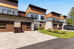 A modern multi-story residential building with a stone facade, large windows, and a paved driveway. - 3 BR townhouse with balcony - fireplace - near beach (Lake George)