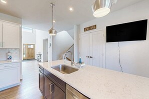 A modern kitchen with a white countertop, stainless steel sink, and a flat-screen TV mounted on the wall. - 3 BR townhouse with balcony - fireplace - near beach (Lake George)