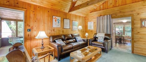 A wooden interior with a sofa, chairs, a coffee table, and a ceiling fan.