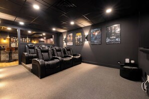 Une salle de cinéma privée avec un intérieur sombre, des fauteuils en cuir inclinables et des affiches de films accrochées au mur.