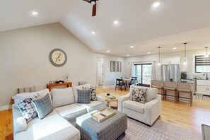 A spacious living area with a high ceiling, a dining area, and a kitchen with modern appliances. - New 5-BR Home with Movie Theater, Bar, Game Room (Lake George)