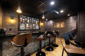 A bar area with wooden bar stools, a brick wall, and a mural of beer glasses. - New 5-BR Home with Movie Theater, Bar, Game Room (Lake George)
