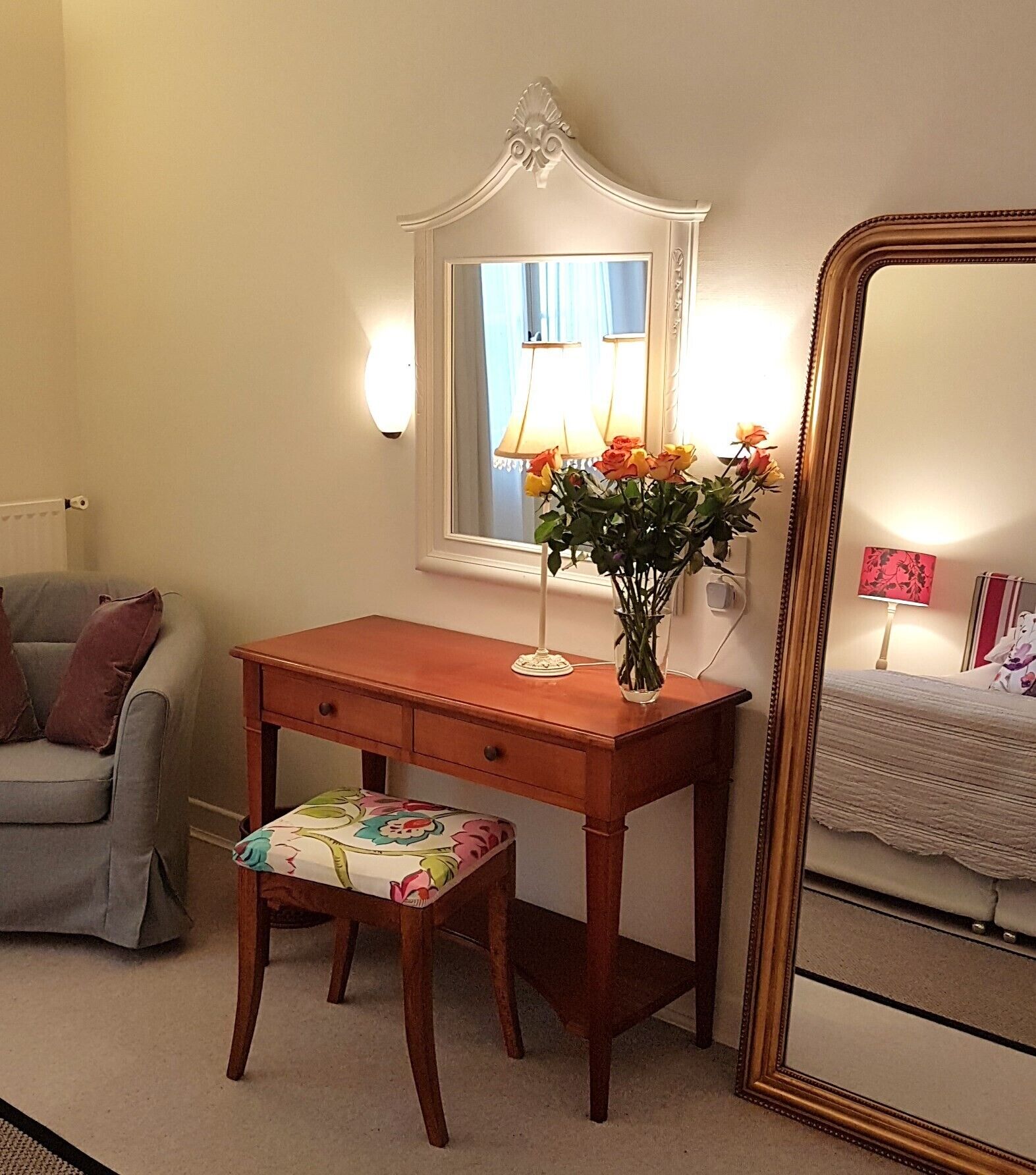 A room with a wooden desk, a chair, a mirror, and a lamp.