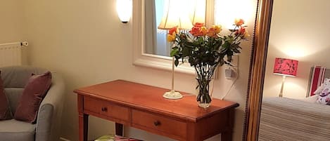 Una habitación con un escritorio de madera, una silla, un espejo y una lámpara.