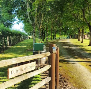 Ein Baumweg mit hölzernem Zaun und einem Schild, auf dem 'Domaine de Leygue' steht.