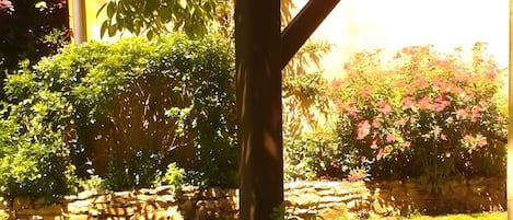 Un jardín con muro de piedra, pérgola de madera y diversas plantas y flores.