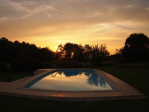 A rectangular swimming pool with a ladder, surrounded by a paved deck, set against a sunset sky. - Holiday Home 'Grace's Gate At Domaine De Leygue' with Wi-Fi (Bourniquel)