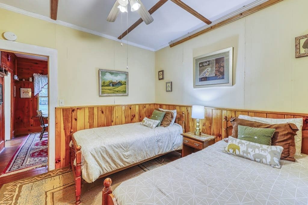 Une chambre avec deux lits, des têtes de lit en bois, une table de chevet, une lampe et un tableau au mur.
