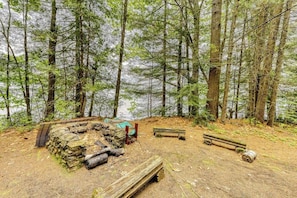 Ein bewaldetes Gebiet mit einer Steinstruktur, hölzernen Bänken und einer kleinen Holzbrücke.