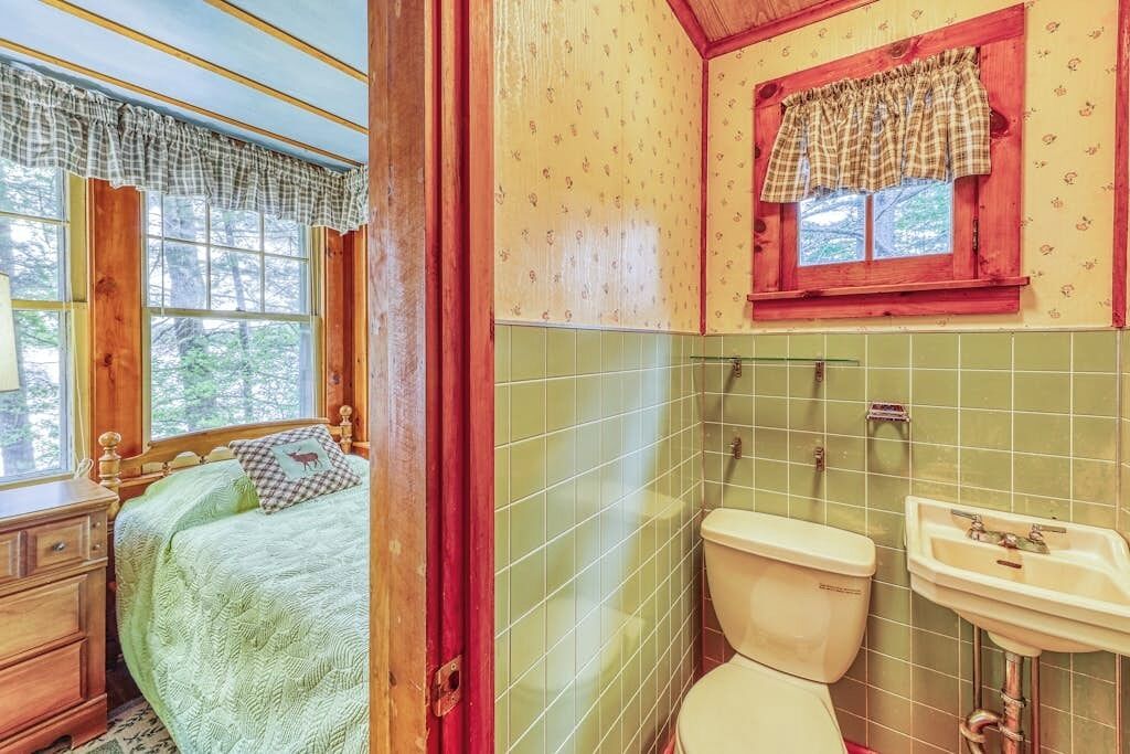 Une pièce comprenant un lit, une fenêtre avec des rideaux, des toilettes et un lavabo.