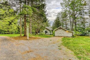 Uma cabana rústica com entrada por caminho de pedras, rodeada por árvores densas.