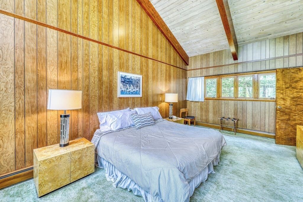 Une chambre à coucher avec un grand lit, des murs en bois et une fenêtre avec des rideaux.