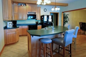 A kitchen with wooden cabinets, a black refrigerator, a sink, and a bar stool.