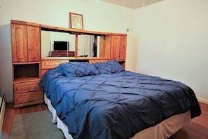 A bedroom with a bed, wooden wardrobe, and a mirror.