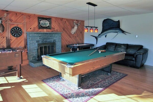 A pool table with a dartboard, a fireplace, and a mounted deer head.