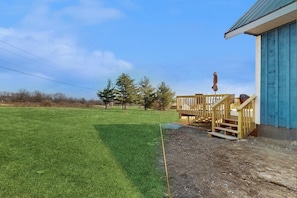 A grassy outdoor area with a wooden deck and a building with a blue door. - 1BR vineyard stay with firepit, grill, & EVC (Keuka Park)