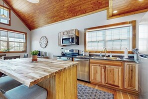 Une cuisine avec des meubles en bois, un îlot central intégré, des appareils électroménagers en acier inoxydable et une grande fenêtre.