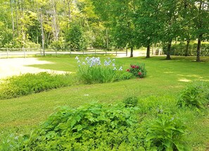 A well-maintained garden with various plants and flowers, a paved walkway, and trees in the background. - Holiday Home 'Barn Cottage' with Wi-Fi (Bourniquel)