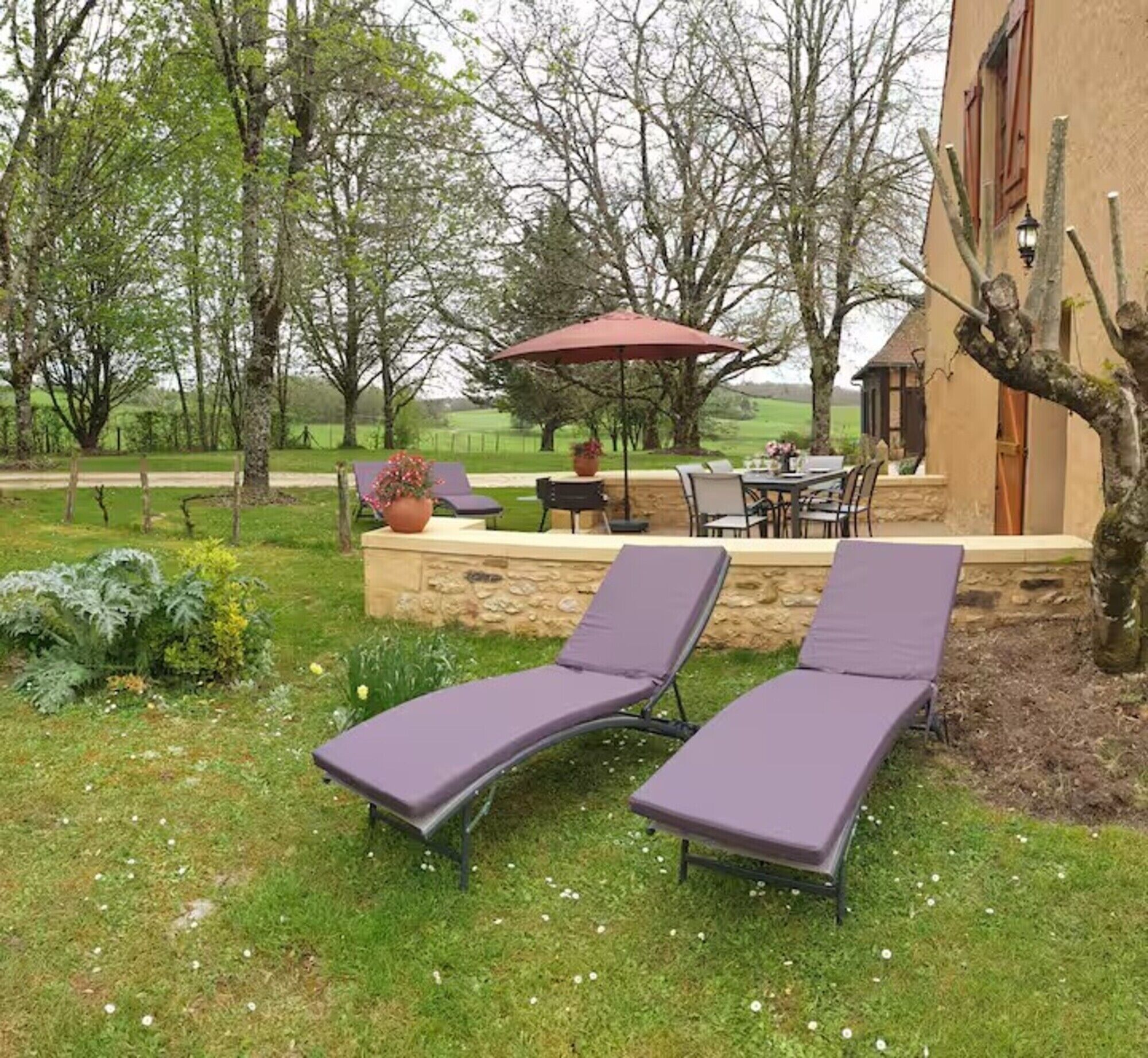 Eine Terrassenfläche mit zwei Liegestühlen, einem Tisch und einem roten Sonnenschirm.
