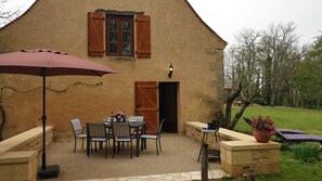 A rustic building with a patio area featuring a table and chairs, a wooden door, and a potted plant. - Holiday Home 'Barn Cottage' with Wi-Fi (Bourniquel)