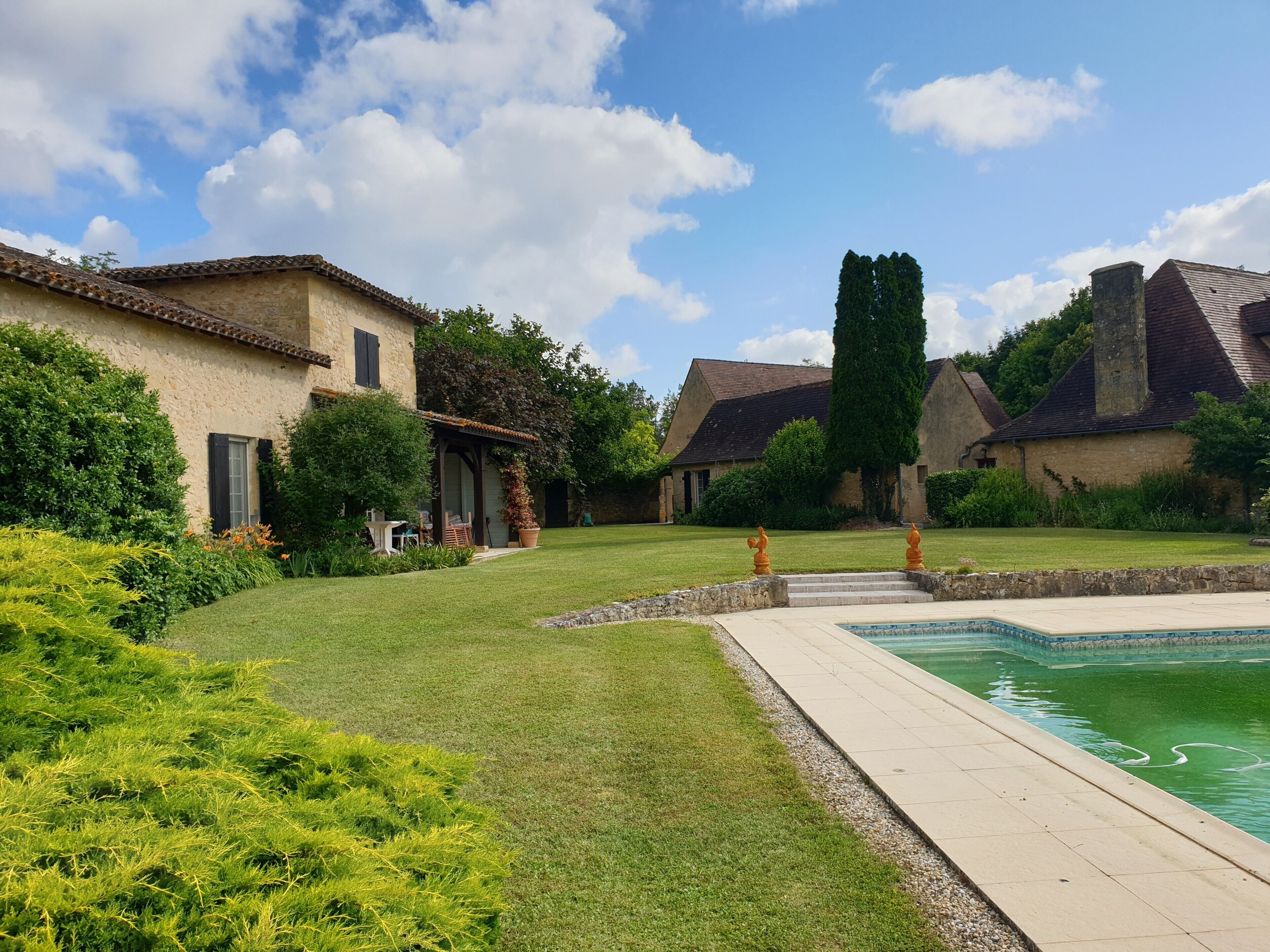 Une cour avec une piscine, des bâtiments en pierre et une pelouse bien entretenue.