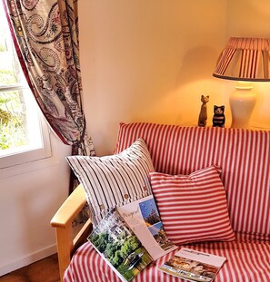 A cozy room with a striped sofa, a wooden side table with magazines, and a lamp. - Holiday Home 'May Cottage At Domaine De Leygue' with Wi-Fi (Bourniquel)