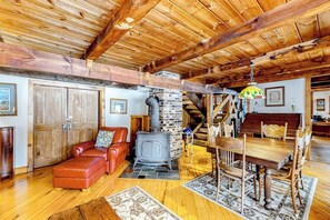 A rustic interior with a wooden ceiling, a brick fireplace, leather seating, and a dining table.