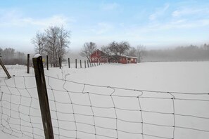 A snow-covered landscape with a red barn and a wooden fence.