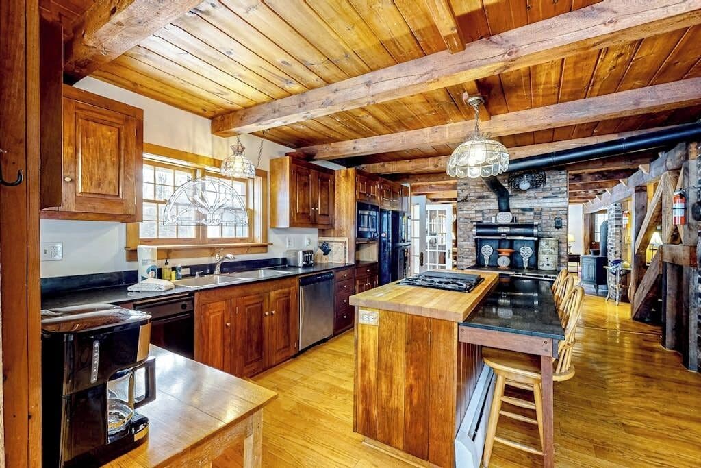 A spacious kitchen with wooden cabinets, a central island, and a stone fireplace.