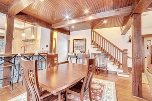 Un vaste espace de salle à manger avec une table et des chaises en bois, une cuisine équipée d’appareils modernes et un escalier menant à un autre niveau.