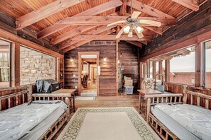 A log cabin interior with two beds, a ceiling fan, and a stone wall. - Luxe 4BR Mountainview Adirondacks (North Creek)