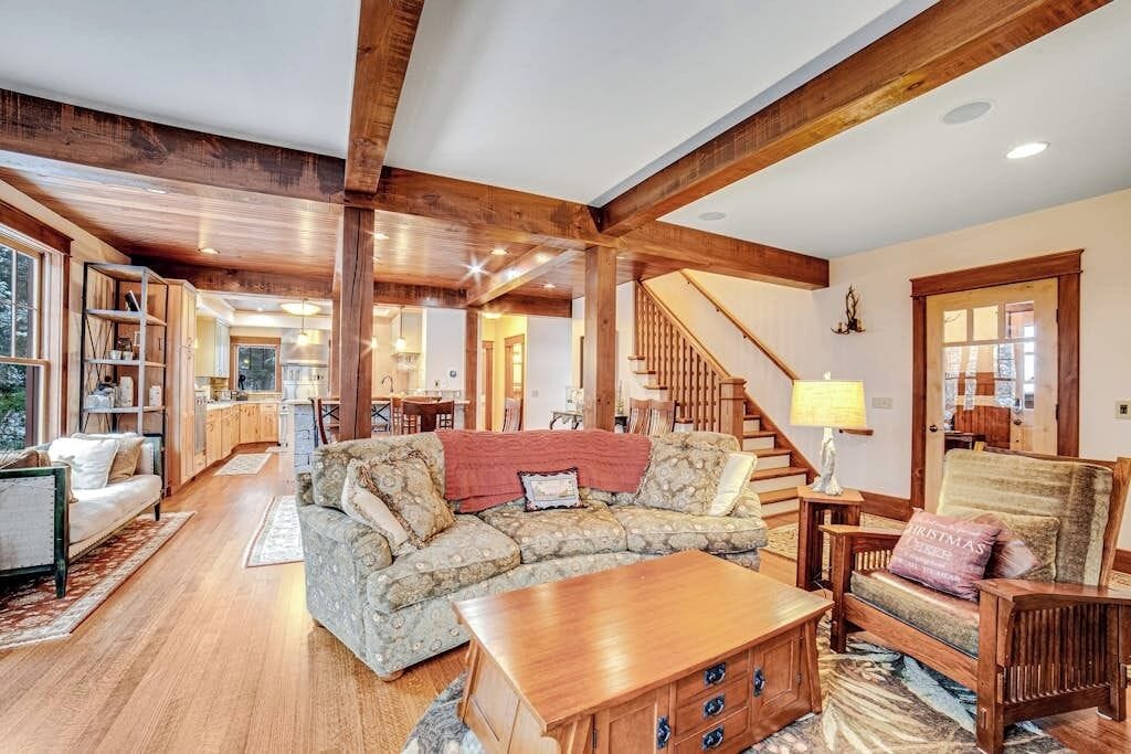 A spacious living room with a wooden staircase, a sofa set, and a dining area.