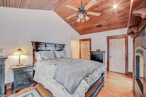 Une chambre à coucher avec un plafond en bois, un lit avec une literie à motifs, une table de chevet, une commode et une porte.