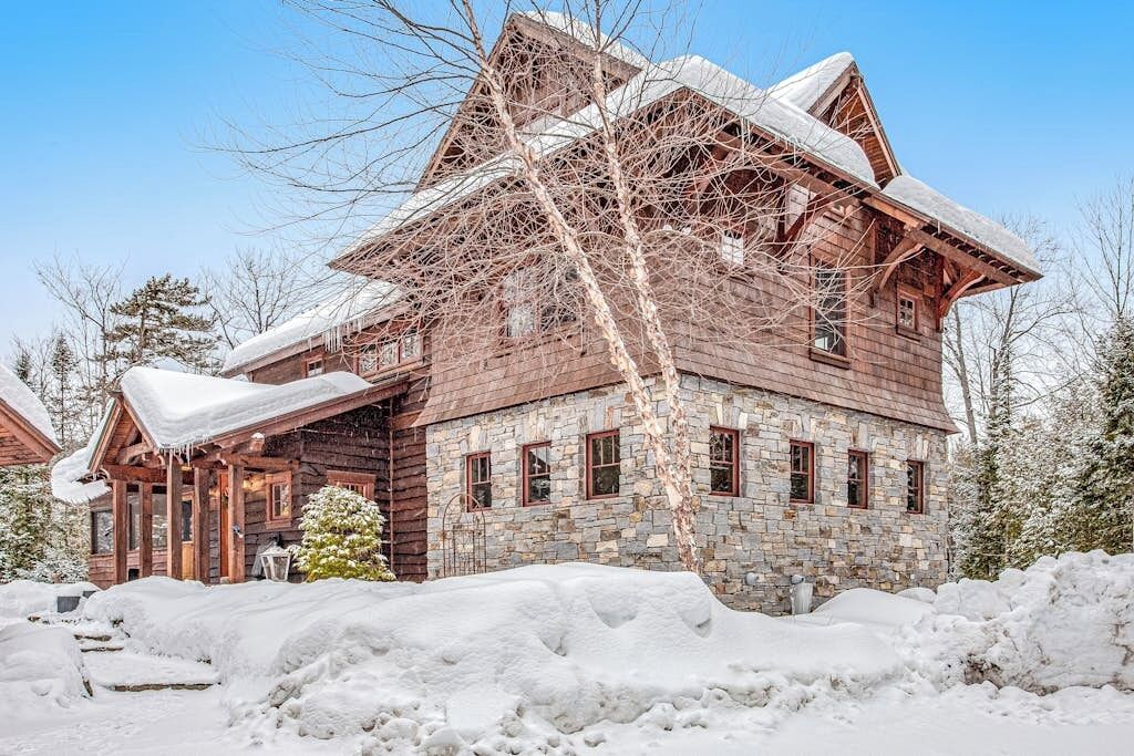 Une cabane en rondins avec des fondations en pierre, de nombreuses fenêtres et un toit recouvert de neige.