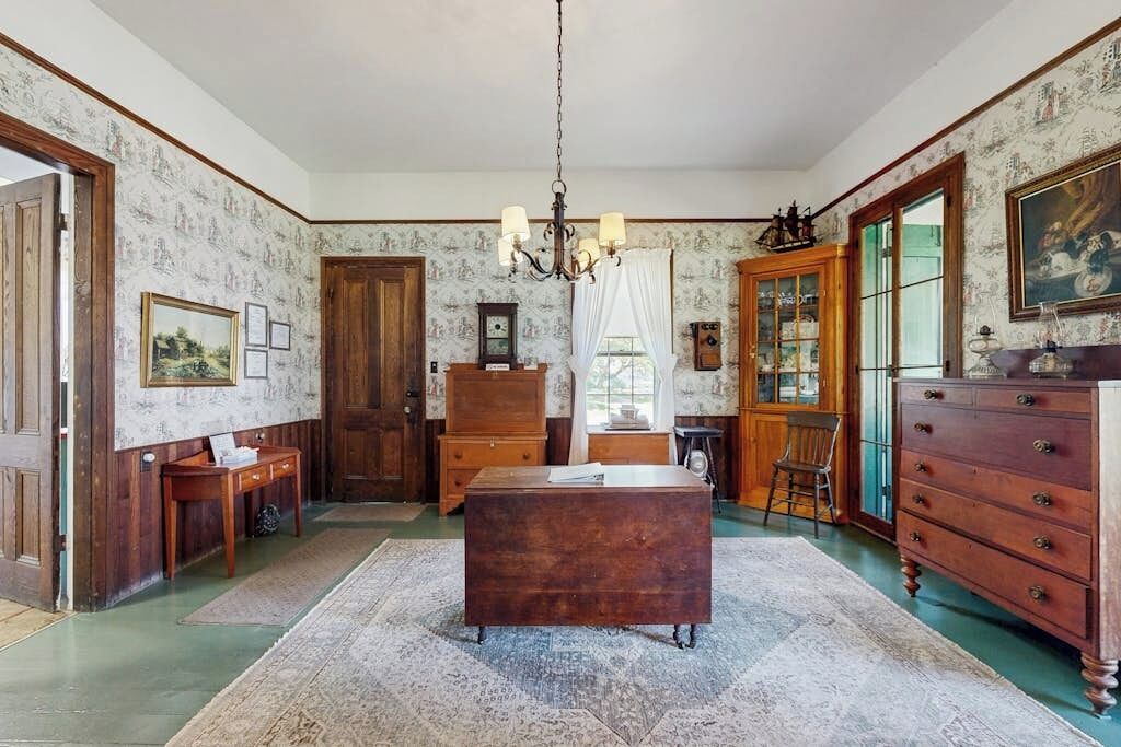 Een kamer met een houten bureau, een kroonluchter, een kast en een groot raam.
