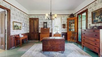 Een kamer met een houten bureau, een kroonluchter, een kast en een groot raam.