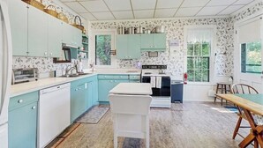 Una cocina con armarios color turquesa, una encimera blanca y una zona de comedor con mesa y sillas.