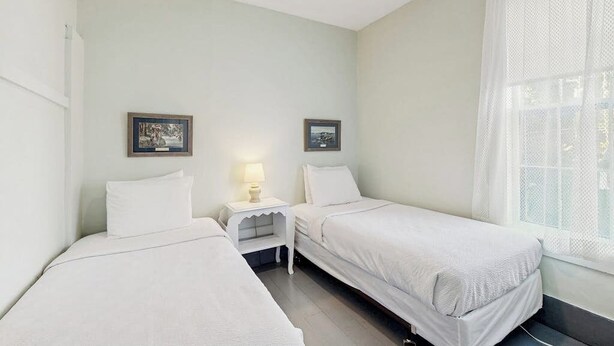 A room with two single beds, a small bedside table with a lamp, and a window with sheer curtains. - Gorgeous, dog-friendly 6BR with amazing views (Rock Stream)