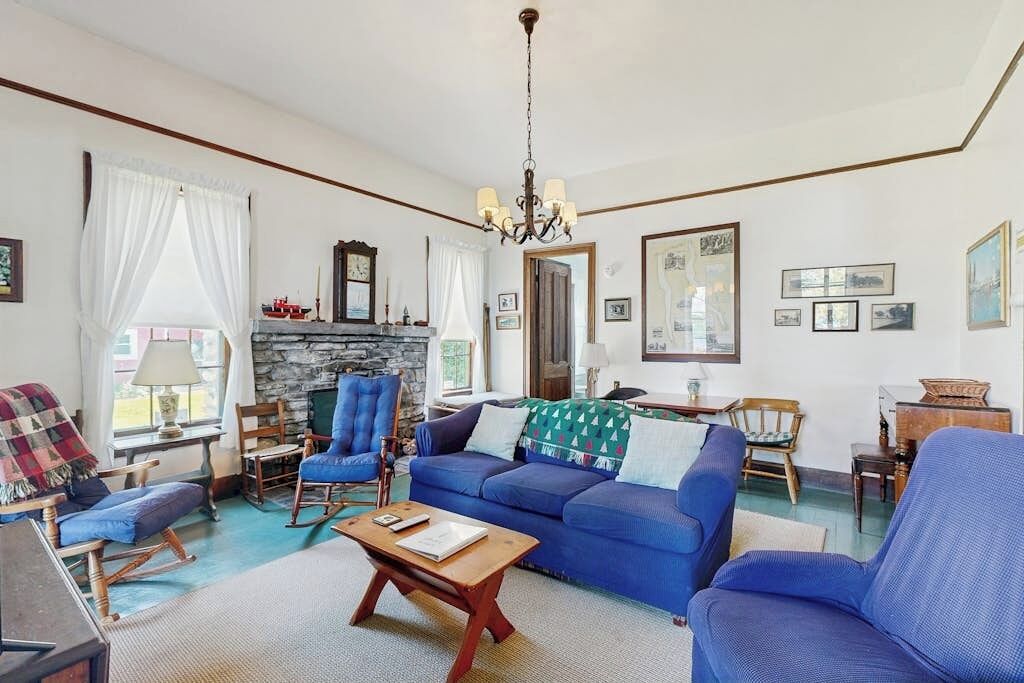 Een woonkamer met een blauwe bank, een houten salontafel, een stenen open haard en een kroonluchter.