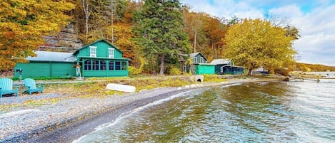 En fastighet vid vattnet med en brygga, en miljövänlig byggnad och en skogbeklädd sluttning.
