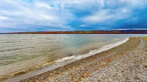 Una playa pedregosa con aguas cristalinas y una vista distante de un paisaje boscoso bajo un cielo nublado.