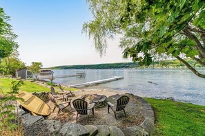 A lakeside outdoor seating area with chairs and a fire pit, overlooking a calm lake. - Keuka Vista|Lakefront 4BR with amazing views, dock & game room (Penn Yan)