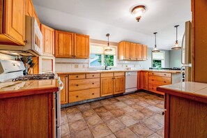 A kitchen with wooden cabinets, a dishwasher, and a tiled floor. - Keuka Vista|Lakefront 4BR with amazing views, dock & game room (Penn Yan)