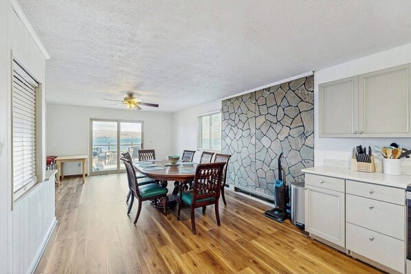 A dining area with a wooden table and chairs, a stone wall, and a view through the window.