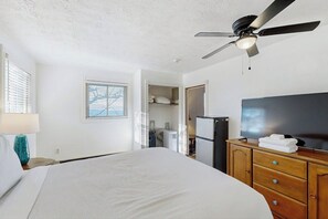 A hotel room with a bed, a ceiling fan, a TV, a dresser, and a window with blinds.