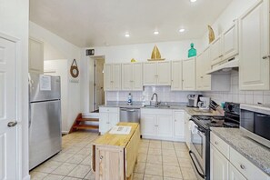 A compact kitchen with white cabinets, a stainless steel refrigerator, a stove, and a sink.