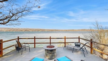 A deck with outdoor seating and a fire pit overlooking a body of water.