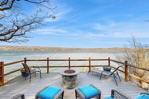 A deck with outdoor seating and a fire pit overlooking a body of water.