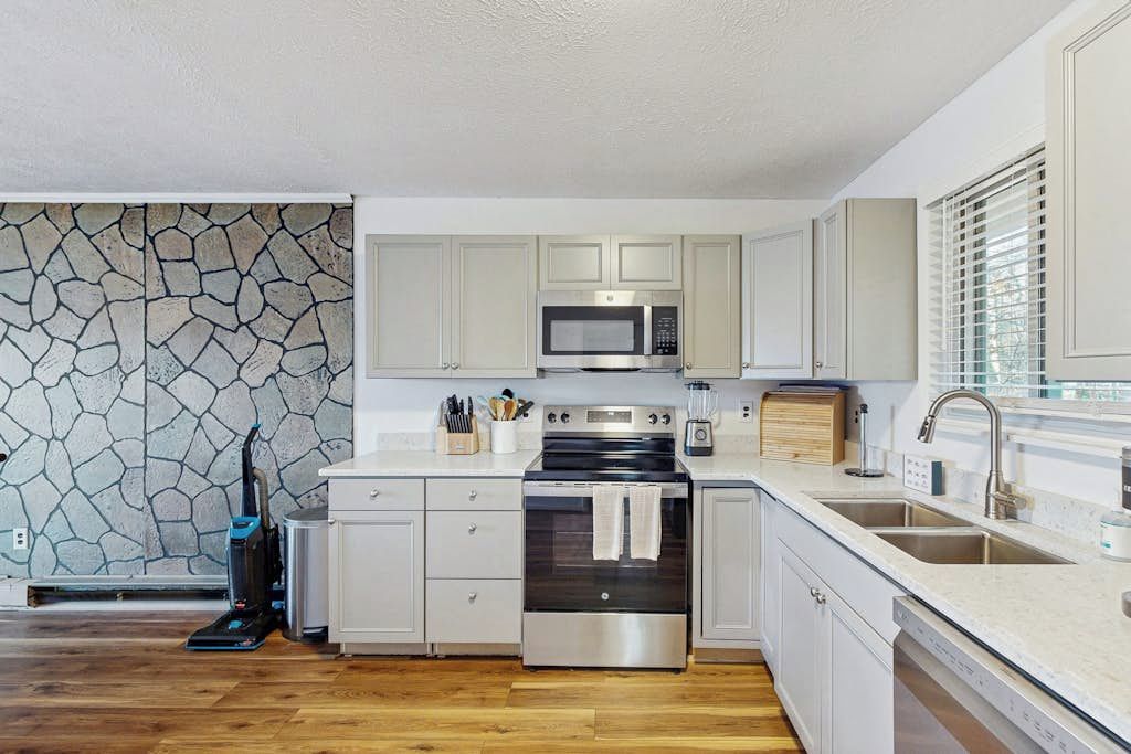 A modern kitchen with white cabinetry, a stone backsplash, a built-in microwave, a stove, and a dishwasher.