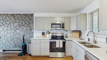 A modern kitchen with white cabinetry, a stone backsplash, a built-in microwave, a stove, and a dishwasher.